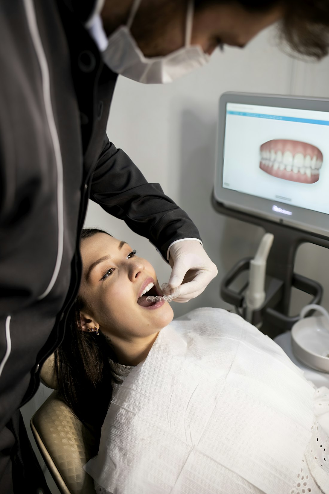Dentist fitting a patient with clear aligners beside a 3D scan on screen